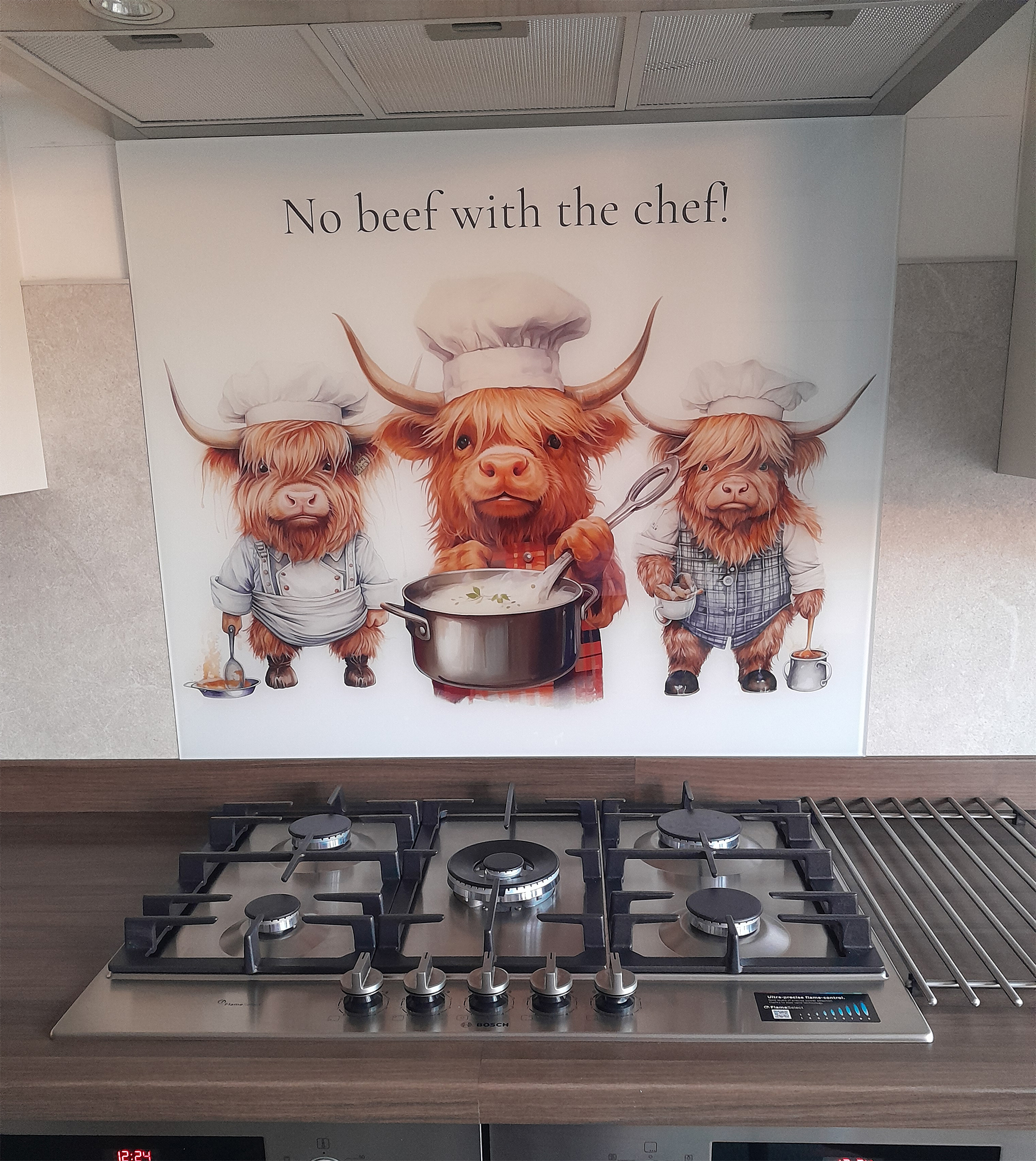 Printed glass kitchen splashback featuring three cute Highland cow chefs on a white background with the quote “No beef with the chef!” above a gas hob.