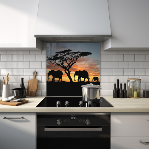 Family of elephants walking by tree silhouetted against sunset glass splashback.